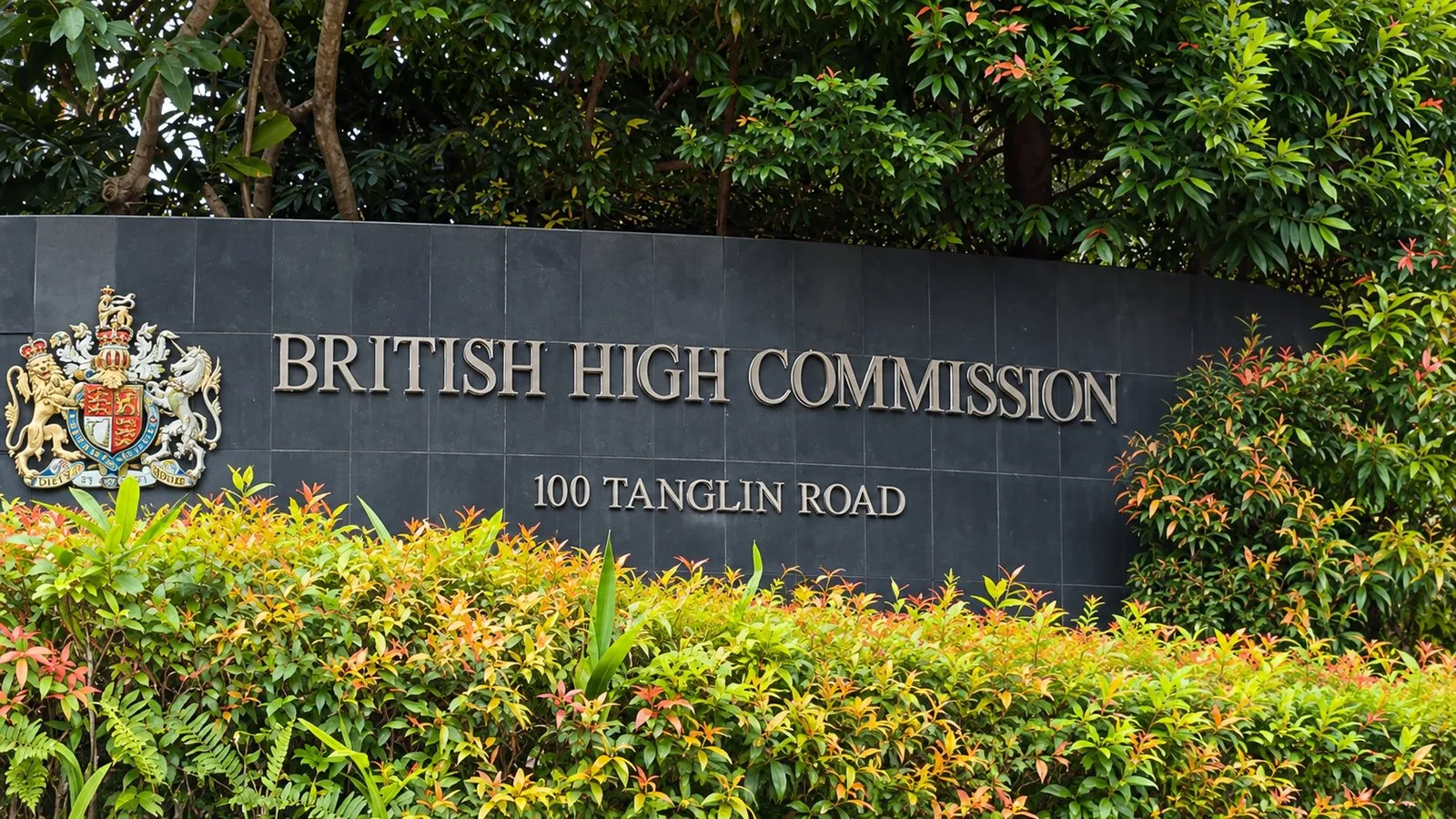 The British High Commission sign with the royal coat of arms at 100 Tanglin Road, Singapore, framed by tropical shrubs
