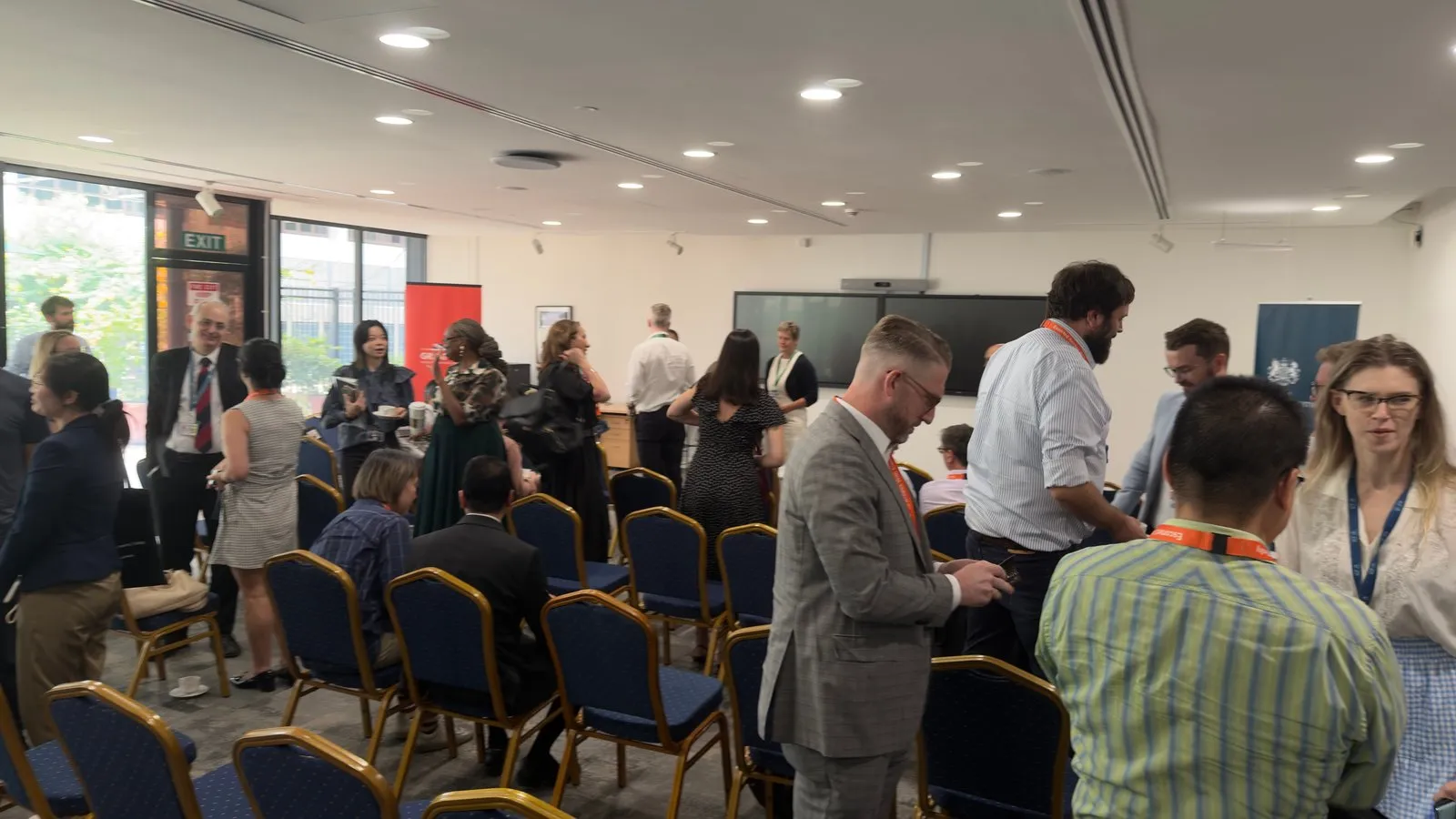Guests talking among rows of chairs in an event room at the British High Commission, with red and navy banners at the back of the room