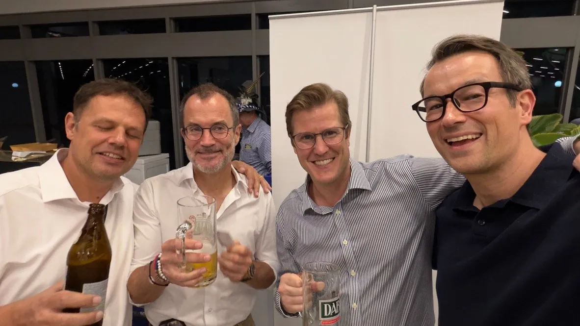 Four guests at the German Centre Oktoberfest smiling together, three of them holding beer bottles and glasses